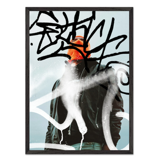 Urban photography of man wearing an orange beanie and black jacket with abstract art graffiti elements on a light blue background. Displayed in a black wooden frame.
