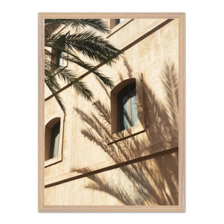 Framed photograph of a minimalist white building with palm tree shadows cast across the surface, displayed in a premium oak wooden frame — perfect for modern coastal and urban interiors