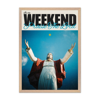 Bold typography poster with a religious figure Jesus with arms outstretched against a blue sky, text 'It's the Weekend Praise The Lord' at the top. Displayed in a premium oak wooden frame.