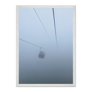 Framed photograph capturing a cable car in misty, foggy conditions, displayed in a premium white wooden frame.