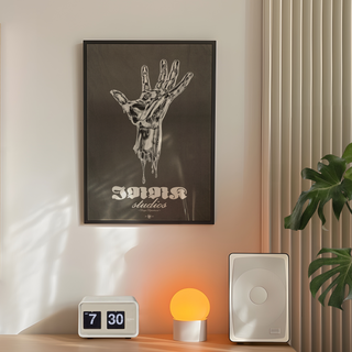 Black and white illustration of a melting silver hand on a black background with 'Innk Studios' branding in white text. Displayed in a black wooden frame. Placed in minimal decor room next to a plant, speakers and lamp.