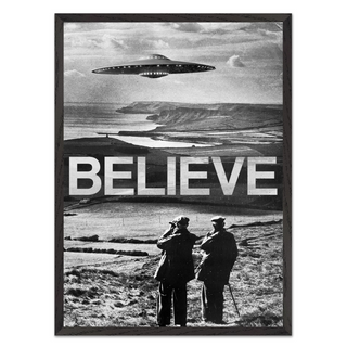 Black and white photography surreal poster with a UFO over a landscape and the word 'BELIEVE' below. Displayed in a black wooden frame.