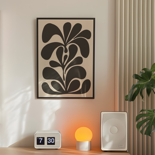 Bold abstract black floral botanical pattern illustration on beige background displayed in a premium black wooden frame. Placed on a wall in a bedroom next to plant, speakers and lamp.