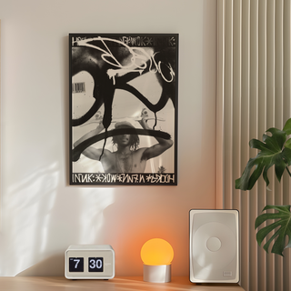 Black and white graffiti poster featuring a man holding a skateboard. Urban style photography paired with graffiti tags in a poster design. Displayed in a premium black wooden frame. Placed in a minimalistic bedroom next to plant, speakers and lamp.