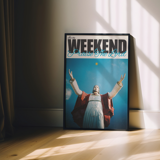 Bold typography poster with a religious figure Jesus with arms outstretched against a blue sky, text 'It's the Weekend Praise The Lord' at the top. Displayed in a premium black wooden frame.