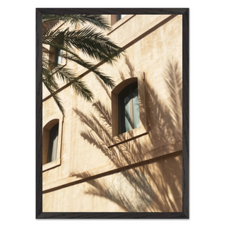 Framed photograph of a minimalist white building with palm tree shadows cast across the surface, displayed in a premium black wooden frame — perfect for modern coastal and urban interiors