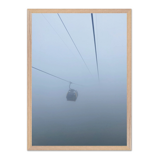 Framed photograph capturing a cable car in misty, foggy conditions, displayed in a premium oak wooden frame.