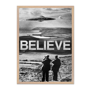 Black and white photography surreal poster with a UFO over a landscape and the word 'BELIEVE' below. Displayed in a black oak frame. 