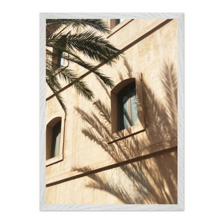 Framed photograph of a minimalist white building with palm tree shadows cast across the surface, displayed in a premium white wooden frame — perfect for modern coastal and urban interiors