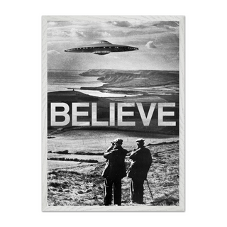 Black and white photography surreal poster with a UFO over a landscape and the word 'BELIEVE' below. Displayed in a white wooden frame. 