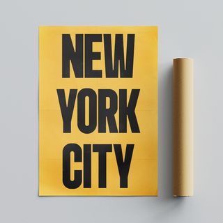 Urban New York poster with black text  'New York City'  on a yellow background. Placed next to cardboard roll tube packaging. 