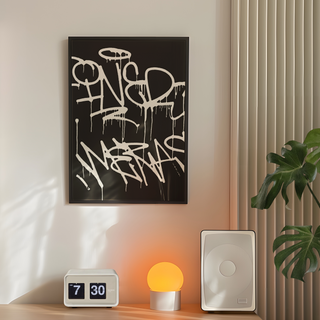 Black and white abstract art print featuring graffiti-style text on a black background, displayed in a premium black wooden frame. Displayed in a bedroom on a wall next to plant, speakers and lamp,. 