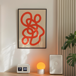 Abstract minimalist print featuring bold red lines on a beige background, displayed in a premium black wooden frame. Placed in bedroom next to plant, speakers and lamp. 