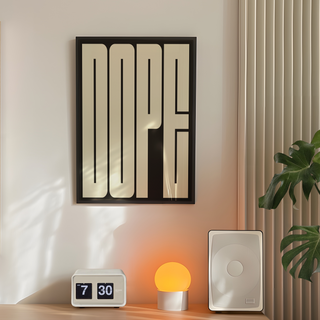 Bold typography poster of cream wording 'DOPE' on black background displayed inn a premium wooden black frame. Placed on the wall in a bedroom next to a plant, lamp and speakers. 